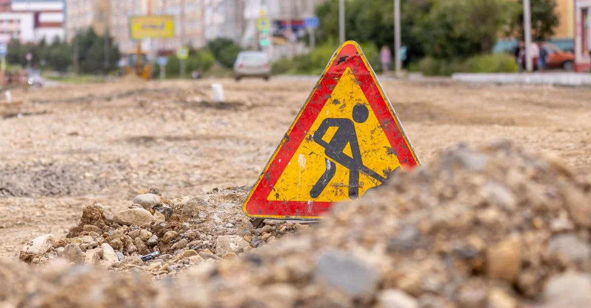 Panneau d'avertissement en forme de triangle jaune indiquant des travaux routiers dans une rue urbaine en construction.