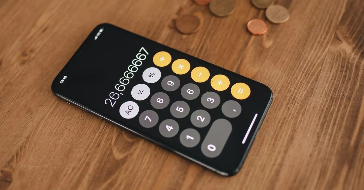 Un gros plan d'un smartphone affichant une application de calculatrice entourée de pièces sur une table en bois.