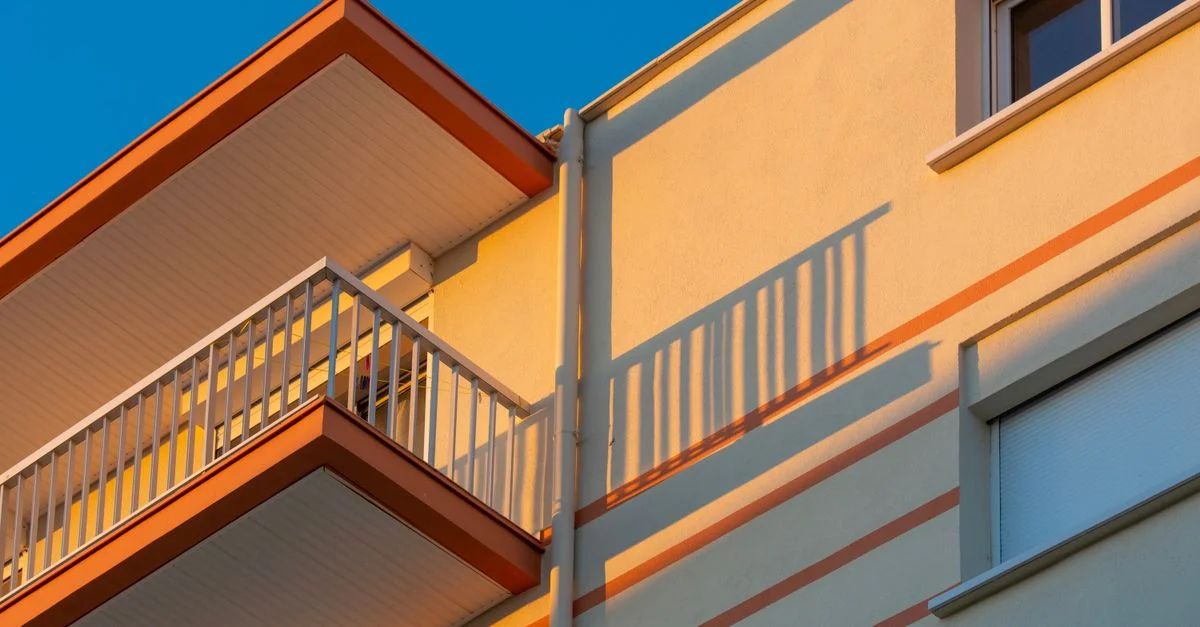 Gros plan de la façade d'un immeuble moderne avec balcons et ombres frappantes éclairées par le soleil.