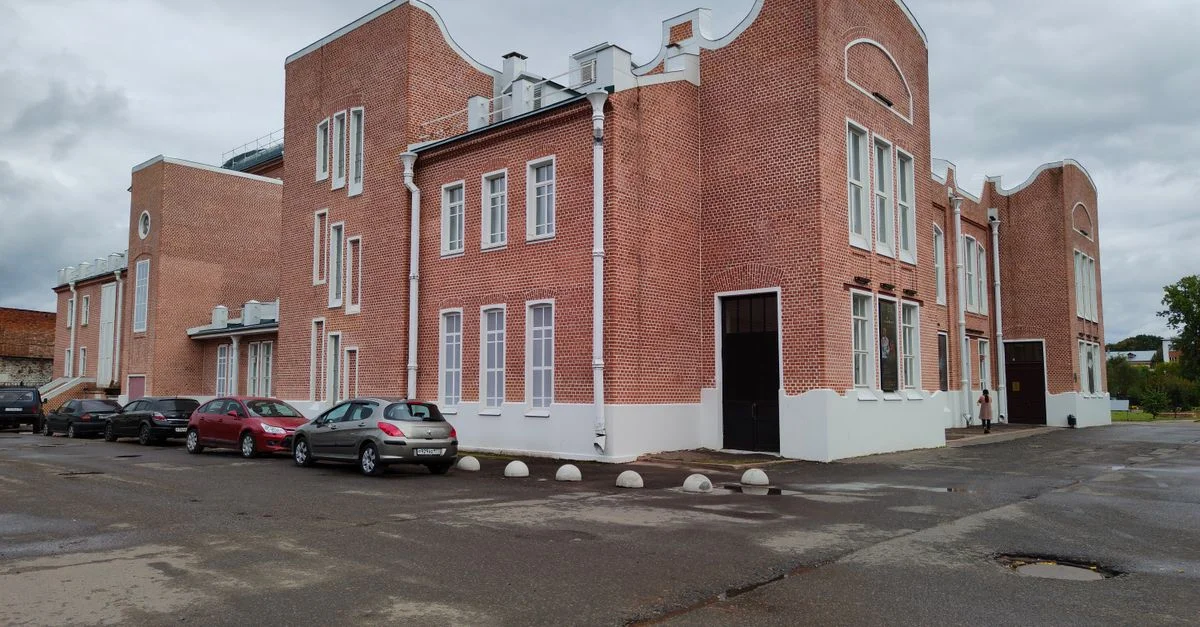 Un extérieur de bâtiment en briques rouges classiques avec des voitures garées à proximité par une journée nuageuse.