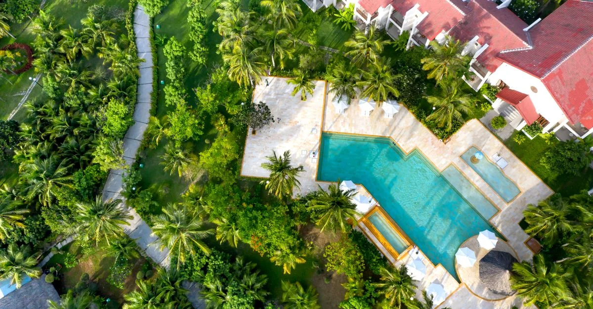 Vue aérienne impressionnante d'une station balnéaire tropicale avec une végétation luxuriante et une grande piscine entourée de villas.