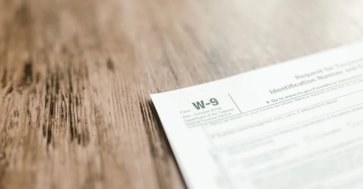 Un gros plan d'un formulaire fiscal W-9 placé sur un bureau en bois, mettant l'accent sur la paperasse et les finances.