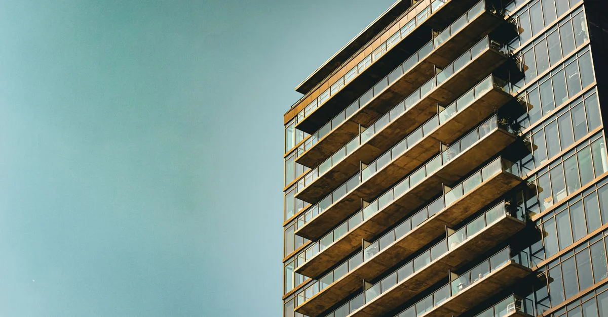 Sleek immeuble d'appartements moderne avec façade en verre et balcons, contre un ciel bleu dégagé.