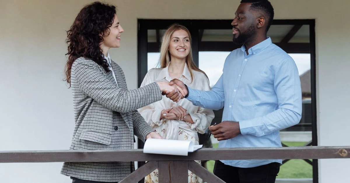 Trois adultes scellant un accord immobilier avec une poignée de main sur un porche.