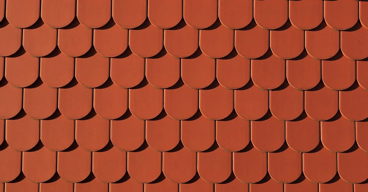 Gros plan sur des tuiles de toit rouges créant un motif uniforme, détail architectural.