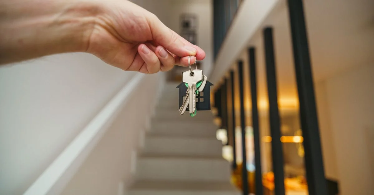 Une main tenant les clés de la maison dans un intérieur moderne, symbolisant l'accession à la propriété ou l'investissement immobilier.