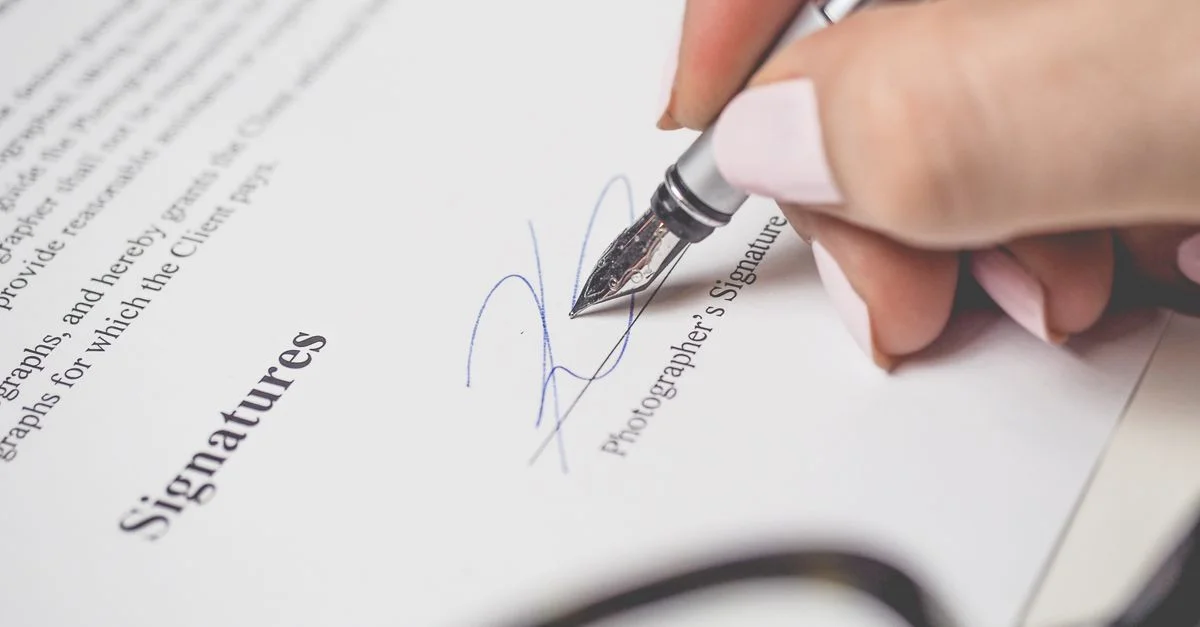 Gros plan sur une main signant un contrat, mettant en valeur un stylo et une écriture élégante.