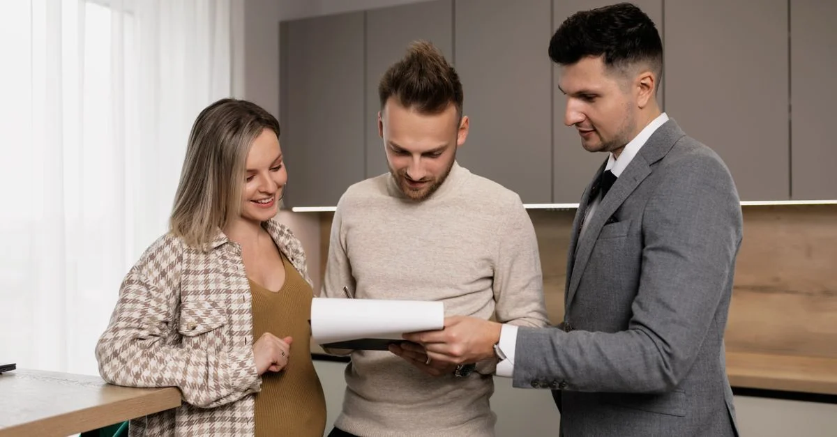 Un agent immobilier présente un contrat de propriété à un jeune couple dans un cadre moderne, discutant des détails.