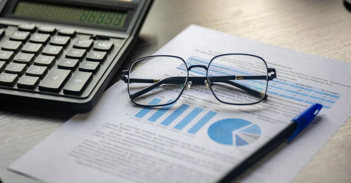 Document financier avec une calculatrice, un stylo et des lunettes symbolisant l'analyse des données.